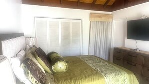 Una camera da letto con un letto, una televisione, una finestra con tende e un soffitto con travi in legno.