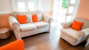 Una sala de estar con un sofá color crema, dos sillones naranjas y un pequeño otoman.