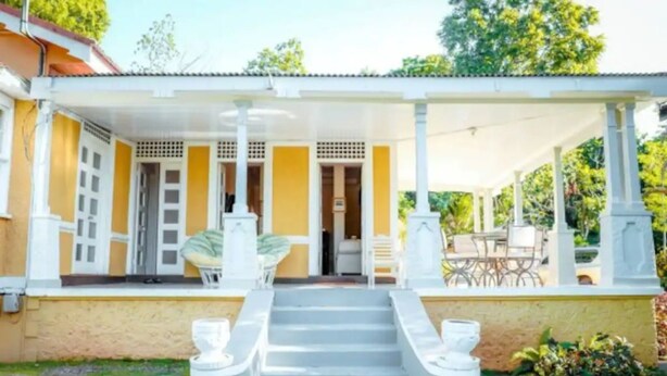 Un edificio de dos pisos con un porche cubierto, columnas blancas y una escalera que conduce a la entrada.