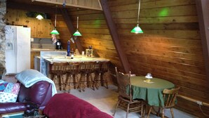 A cozy cabin interior with a wooden dining area, a kitchen, and a seating area with a couch and chairs. - Govy A Frame w/ Hot Tub. (Government Camp)