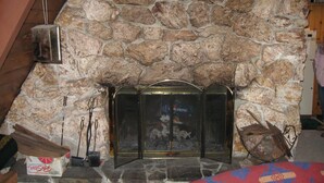 A stone fireplace with a metal screen, a box of tissues, and a wooden box on the floor. - Govy A Frame w/ Hot Tub. (Government Camp)