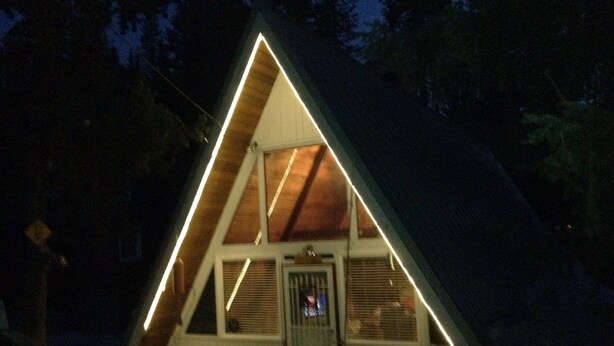 A triangular-shaped cabin with a door and windows, surrounded by trees. - Govy A Frame w/ Hot Tub. (Government Camp)