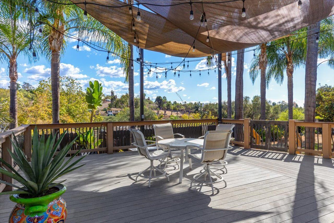 A wooden deck with outdoor furniture, string lights, and a view of palm trees and distant buildings.