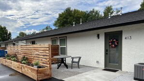 A motel with a number 413 sign, a wooden planter with plants, a small table and chair, and a wreath on the door. - The Benton - Warmly decorated, cozy apartment in downtown Bentonville (Bentonville)