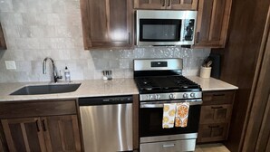 A kitchen with wooden cabinets, a stainless steel dishwasher, a microwave, an oven, and a sink. - The Benton - Warmly decorated, cozy apartment in downtown Bentonville (Bentonville)