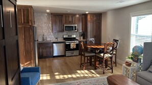 A modern kitchen with wooden cabinets, stainless steel appliances, and a dining area with a round table and chairs. - The Benton - Warmly decorated, cozy apartment in downtown Bentonville (Bentonville)
