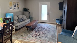A living room with a sofa, coffee table, and a rug. There is a door with a view to the outside. - The Benton - Warmly decorated, cozy apartment in downtown Bentonville (Bentonville)