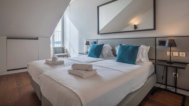 A modern hotel room with a large bed, two pillows, a nightstand, a lamp, and a mirror on the wall. - 8 Building Apartment 403 [T2] - River & Garden View (Lisboa)