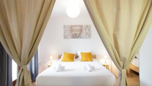 Una habitación de hotel con cama, cortinas, una obra de arte colgada en la pared y dos lámparas de noche.