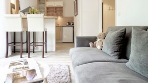 A modern living room with a grey sofa, a coffee table, and a dining area with a kitchen in the background. - L Ourson vue Lac (Annecy)