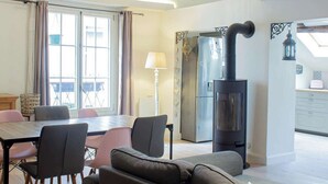 A cozy living room with a fireplace, a dining area with a table and chairs, and a kitchen area with a refrigerator. - Cocoon 1 min romantique (Annecy)