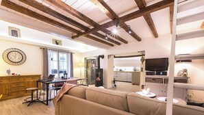 A spacious living area with a wooden ceiling, a sofa, a dining table with chairs, a kitchen in the background, and a fireplace. - Cocoon 1 min romantique (Annecy)