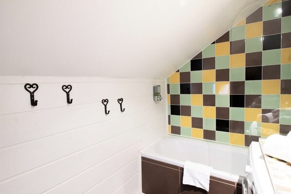 A bathroom with a white tiled wall, a checkered mosaic tile backsplash, and a white bathtub with a towel on it.