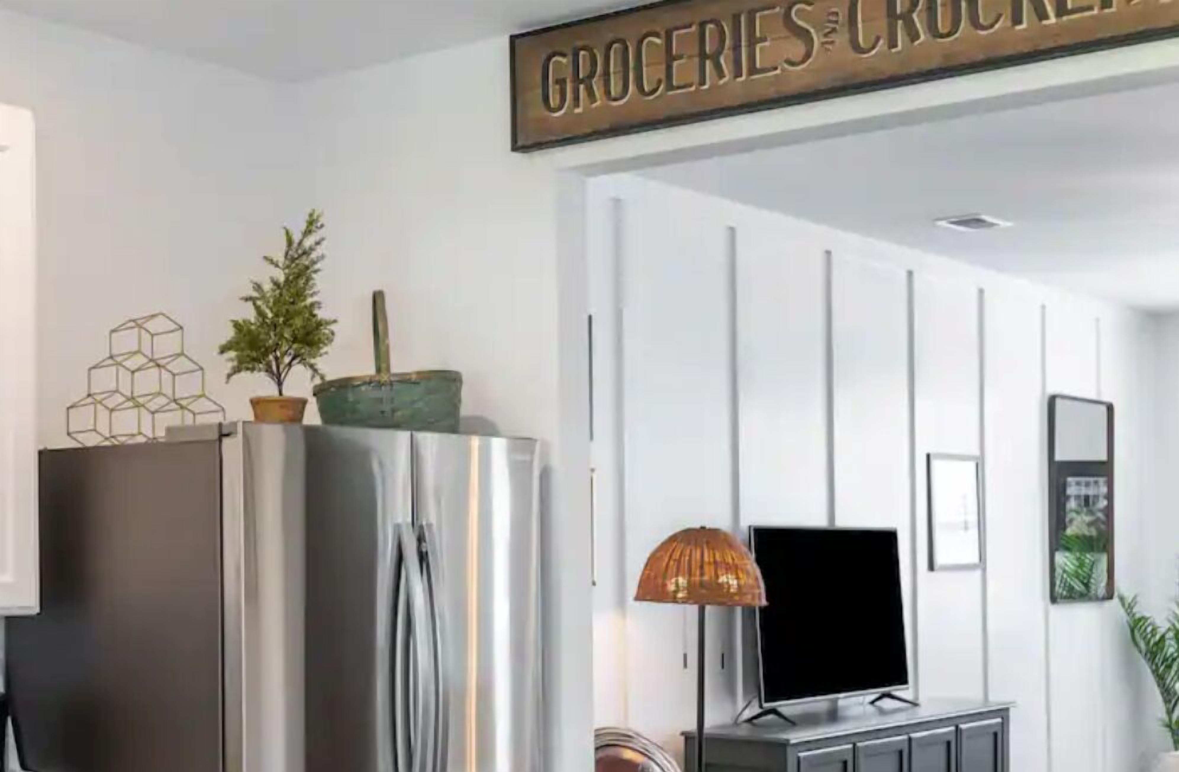 Eine moderne Küche mit einem Edelstahlkühlschrank, einem Blumentopf und einem Schild über der Tür mit der Aufschrift 'GROCERY AND CROCKERY'.