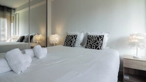 Een moderne hotelkamer met een groot bed, witte lakens en decoratieve kussens.