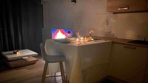 Een compacte keuken met een eettafel, een stoel en een televisie waarop een vlam zichtbaar is.