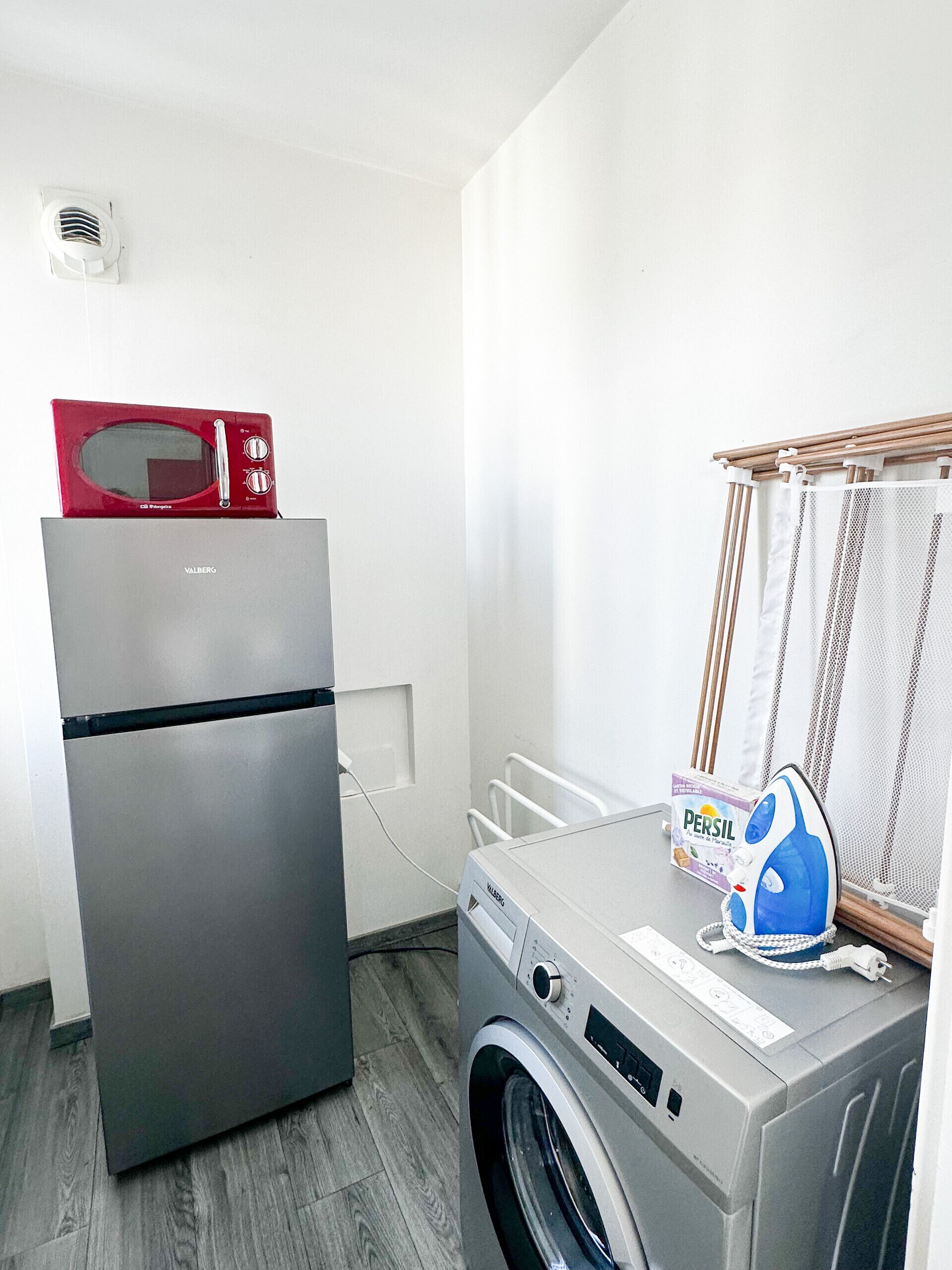 Une petite buanderie équipée d’un lave-linge, d’un sèche-linge, d’un four à micro-ondes et d’une boîte de lessive Persil.