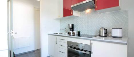 A modern kitchen with white cabinets, a red upper section, a built-in oven, and a coffee maker.