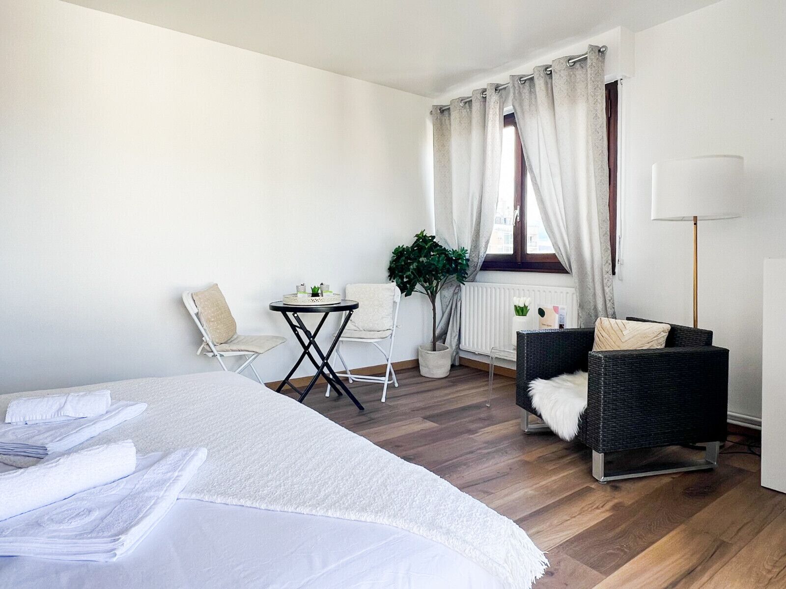 Une chambre d’hôtel avec un grand lit, deux chaises, une petite table, une plante en pot et une lampe sur pied.