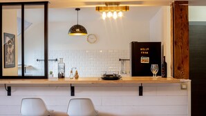A modern kitchen with white subway tiles, a wooden countertop, two white bar stools, a hanging pendant light, and a wine bottle on the counter. - Petit chez-vous pré carré rue Vaugelas (Annecy)