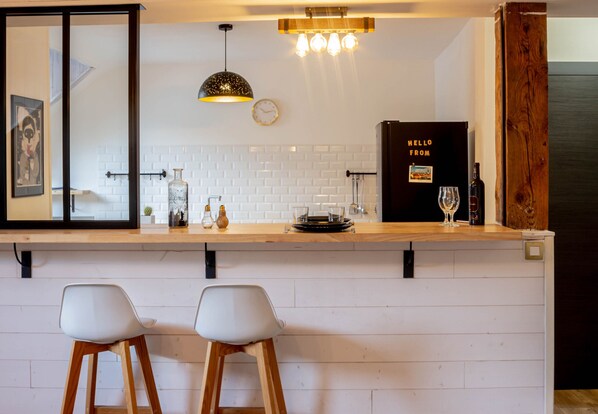 A modern kitchen with white subway tiles, a wooden countertop, two white bar stools, a hanging pendant light, and a wine bottle on the counter.