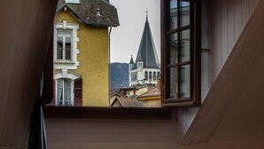 A window with a view of a yellow building and a church steeple. - Petit chez-vous pré carré rue Vaugelas (Annecy)