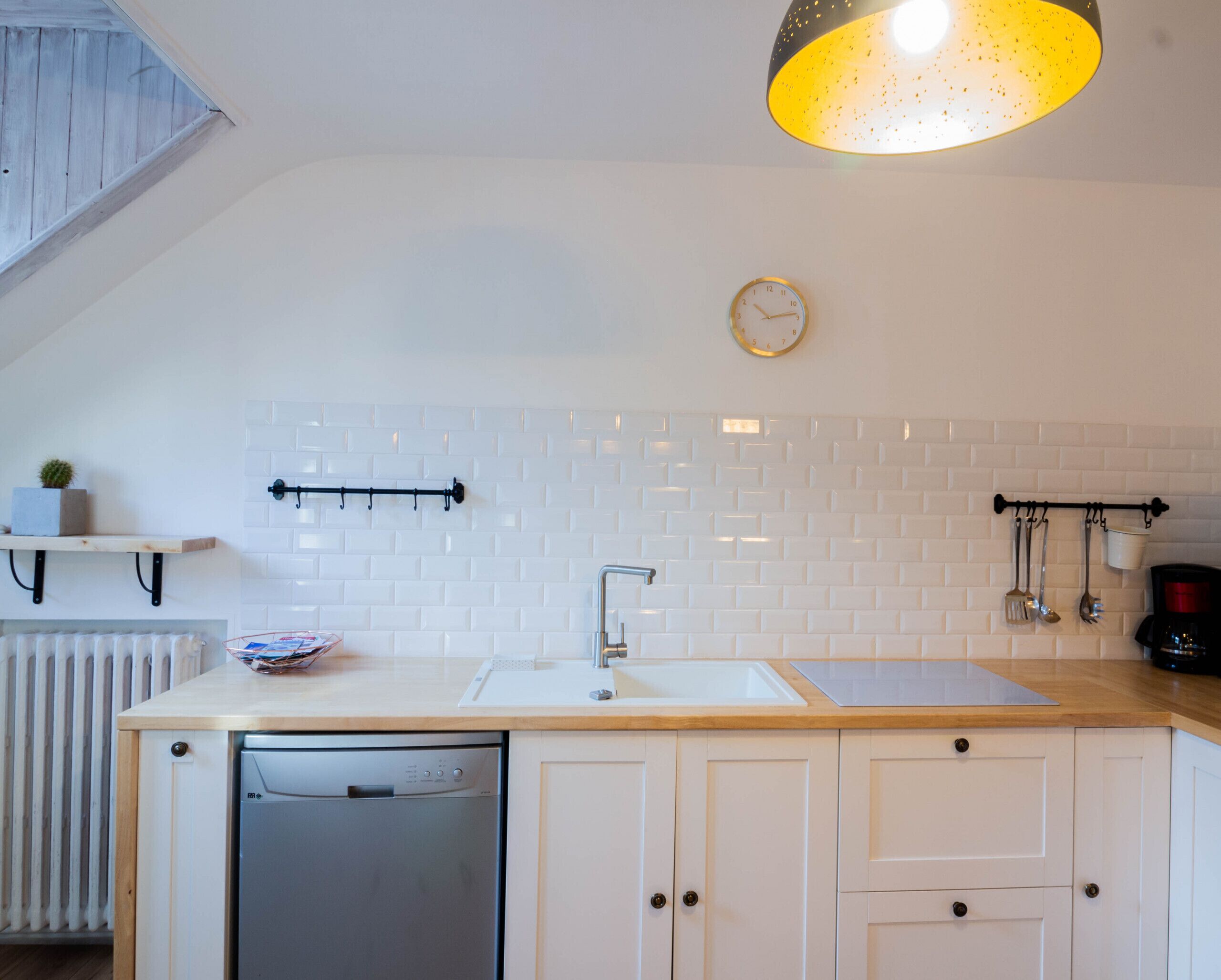 Une cuisine avec des meubles blancs, un lave-vaisselle, un évier et un luminaire suspendu.