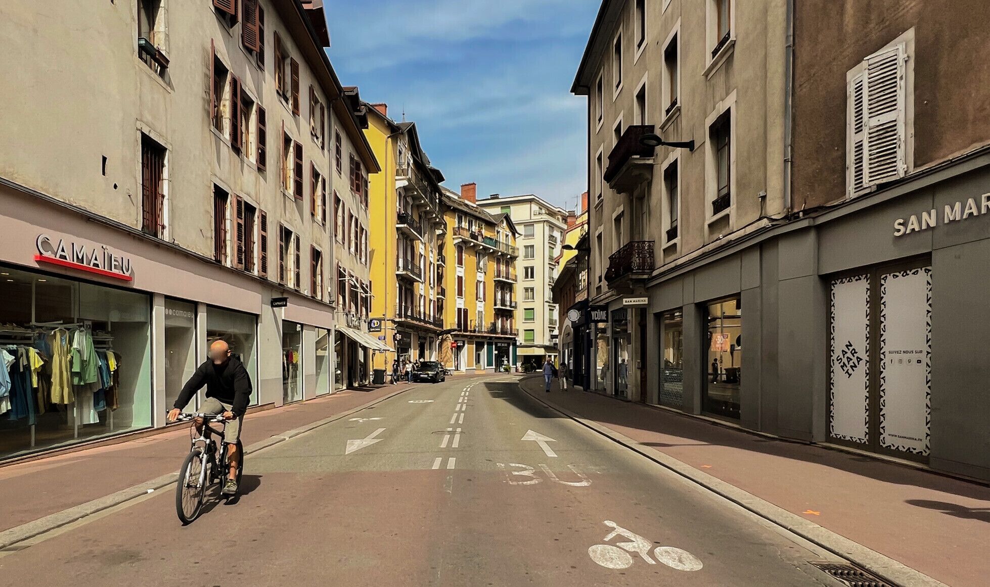 Een straat met gebouwen aan beide zijden, een fietser en een heldere lucht.