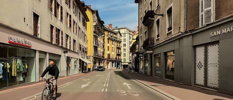 A street with buildings on either side, a cyclist, and a clear sky.