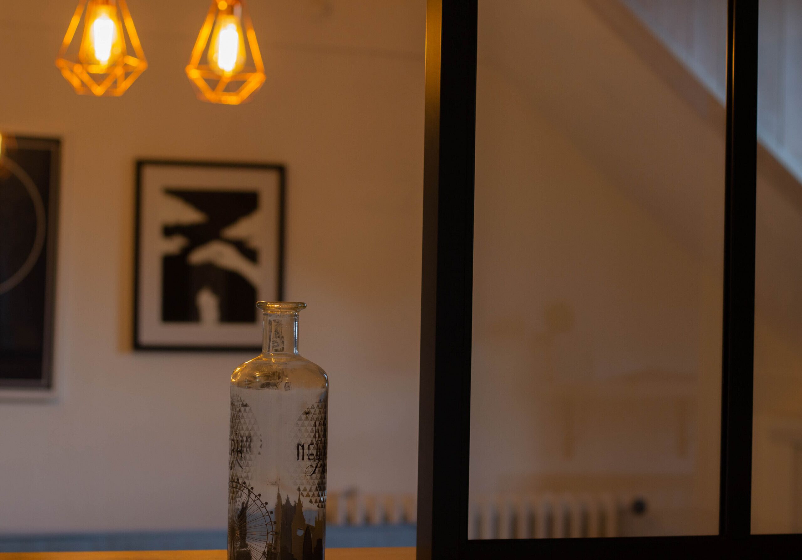A bottle with a label, a framed picture, and two hanging lights.