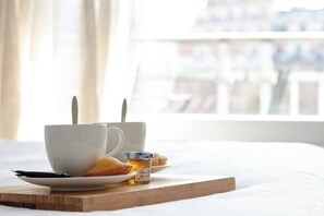 Un plateau de petit-déjeuner comprenant une tasse, une assiette de viennoiseries et un pot de miel, le tout posé sur un plateau en bois sur le lit.