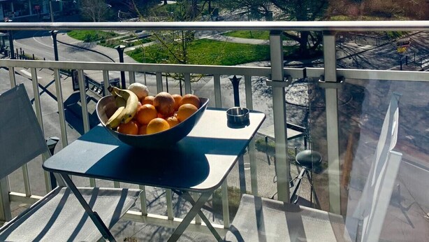 A balcony with a table holding a bowl of fruit, overlooking a cityscape with buildings and a mountain in the distance. - Central Park au centre ville, appareil raclette (Annecy)