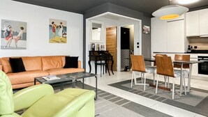Un salon moderne avec un canapé, une table basse et un coin repas comprenant des chaises et une table. On aperçoit une cuisine à l’arrière-plan.