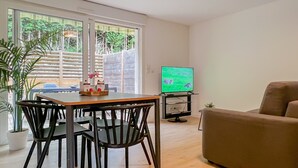 Ein Wohnzimmer mit einem Holzesstisch, schwarzen Stühlen, einem braunen Sofa und einem Fernseher, der eine Naturansicht zeigt.