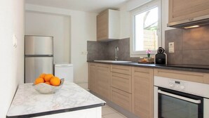Eine moderne Küche mit Marmorarbeitsplatte, einem Edelstahlkühlschrank, Holzschränken und einem eingebauten Backofen.