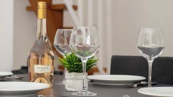 Een eettafel gedekt met een fles wijn, glazen, borden en een kleine pot plant.