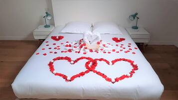 Een keurig opgemaakt bed met rozenblaadjes en twee zwanen, witte kussens en twee bedlampjes.