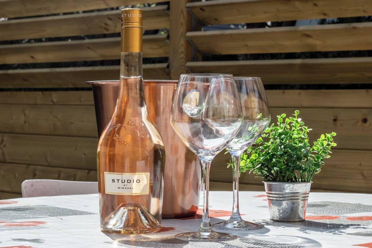 Een fles Studio Miraval wijn, twee wijnglazen en een kleine plant in pot op een buitentafel.