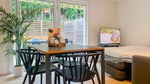 Ein Zimmer mit einem Holztisch, schwarzen Stühlen, einer Couch, einem Fernseher und einer Topfpflanze.