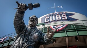 A statue of a man with a microphone, a Cubs logo, and a flag on a building.