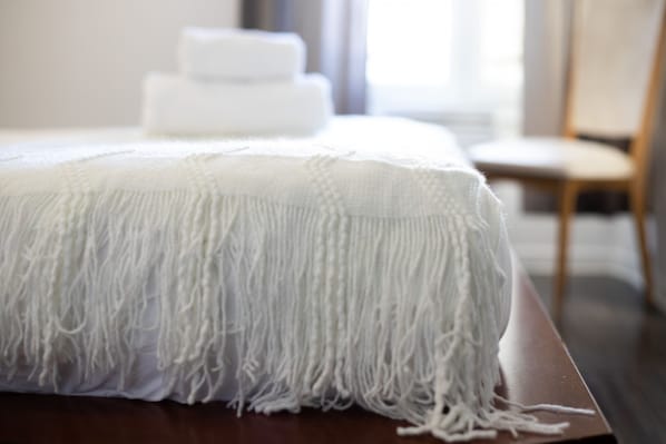 A neatly made bed with a white blanket and a wooden headboard.