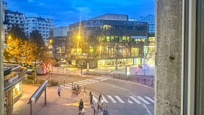 Blick aus einem Fenster auf eine Stadtstraße im Abenddämmerung, mit Gebäuden und einer Fußgängerüberwegung.