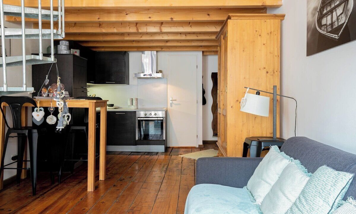 Een gezellige zithoek met een houten plafond, een grijze bank en een keuken op de achtergrond.