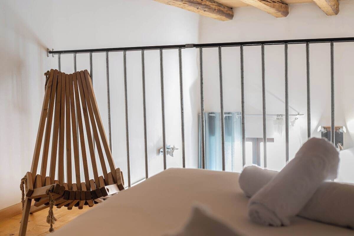 A room with a bed, a wooden swing chair, and a metal railing.