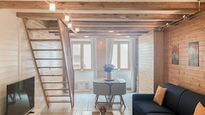 En hyggelig stue med TV, sofa, sofabord og en trappe, der fører op til en etage.