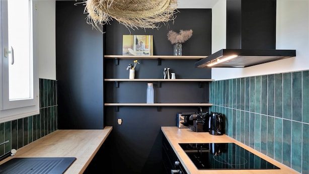 Une cuisine moderne avec des murs noirs, des plans de travail en bois et un dosseret de carrelage vert.