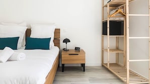 Un letto rifatto con cuscini bianchi e color turchese, un comodino in legno con una lampada e un armadio in legno con ripiani.