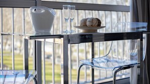 Ein Glastisch mit einer Karaffe, zwei Gläsern und einem Tablett mit Gebäck auf einem Balkon mit Stühlen.