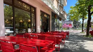 Outdoor seating with red tables and chairs, a storefront with large windows, and a tree with pink blossoms. - Jacuzzi Bay (Annecy)