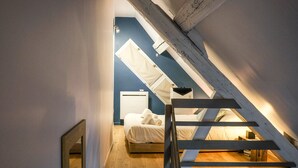 Une chambre avec un plafond en pente, un lit, une table de chevet et une fenêtre.